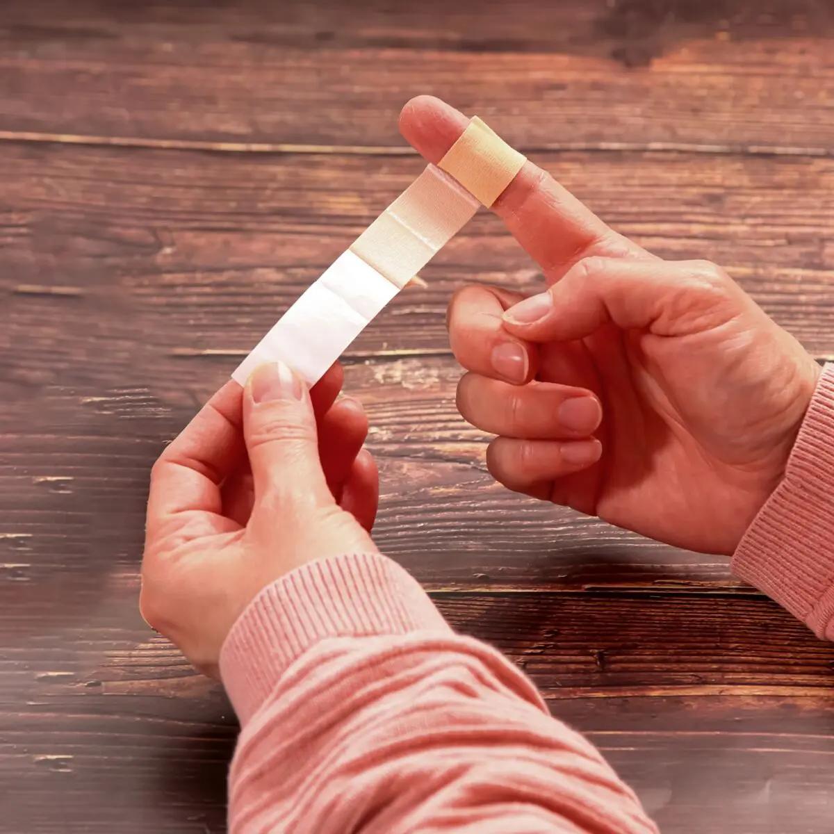 Zwei Hände halten ein Fingerpflaster Weroplast® MasterTex aus weißem, anpassungsfähigem, textilem Gewebe mit cremefarbenem Ende.