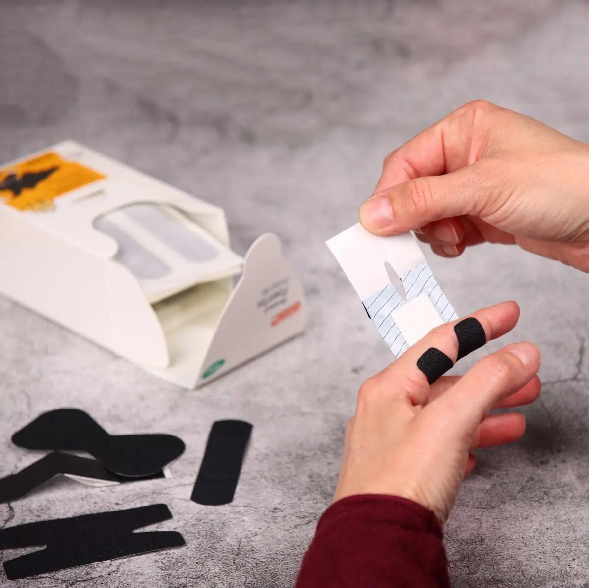 Zwei Hände schneiden ein Stück Weroplast® PowerTex Pflaster - Perfect Mix aus schwarzem, textilem Gewebe mit extra starker Klebkraft und elastischer Struktur.