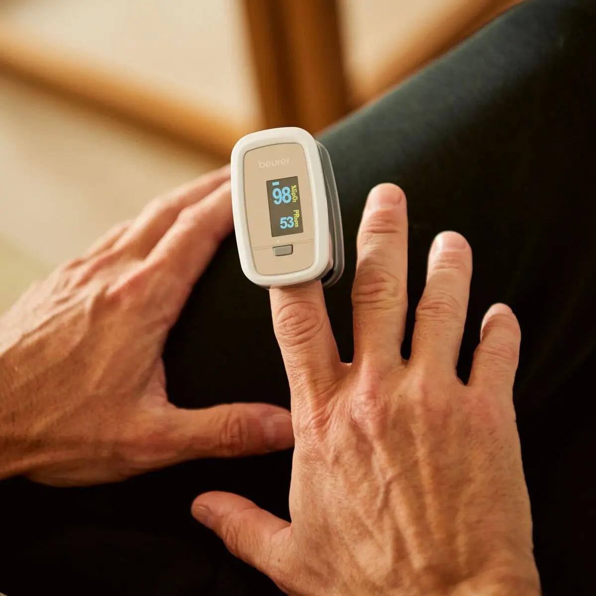 Eine ältere Hand hält ein Beurer Pulsoximeter PO 30, das präzise Sauerstoffsättigung und Puls mit leicht ablesbarem Display misst und besonders kompakt ist.