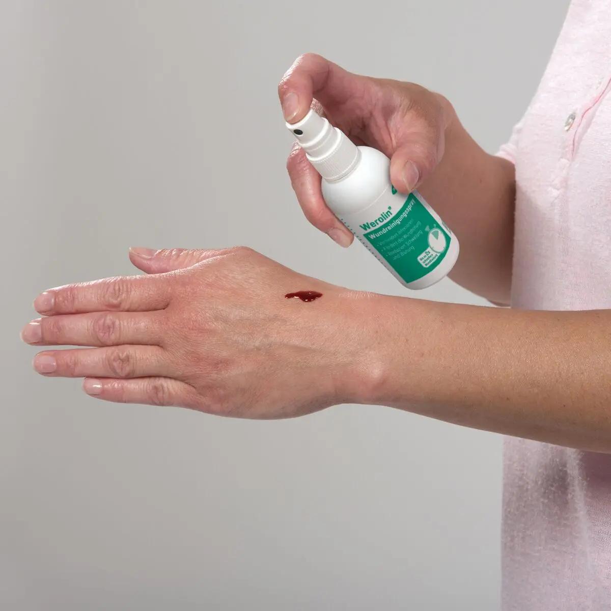 Eine Hand sprüht Werolin® Wundreinigungsspray, 75 ml auf eine kleine Schnittwunde am Handgelenk; alkoholfrei, schmerzfreie Reinigung, reduziert Blutungen.