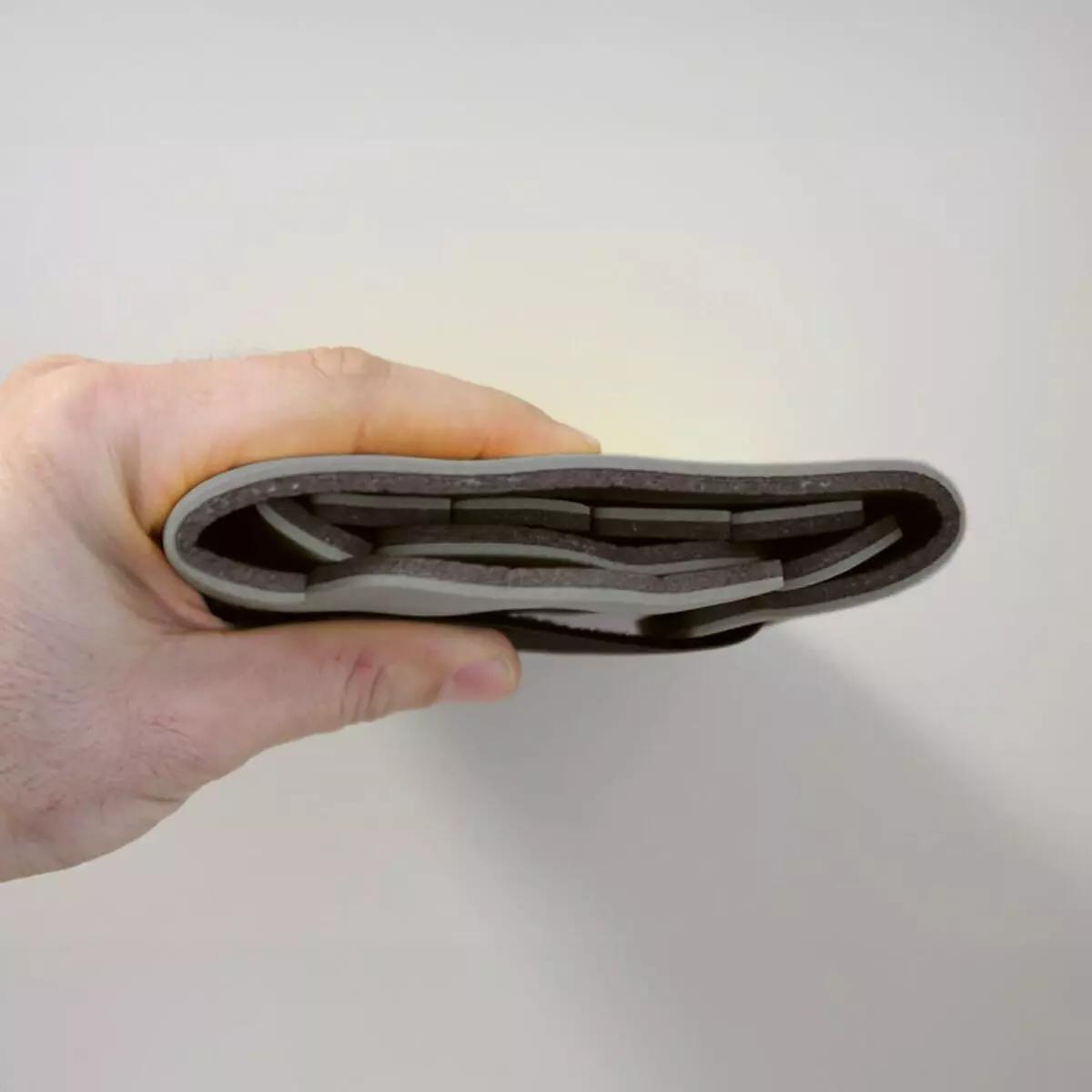 Eine Hand hält einen gefalteten Immobilisationskragen Necklite™ - Grau mit glatter Oberfläche, parallel verlaufenden Aussparungen und flexibler Aluminium-Schaumstoffstruktur.