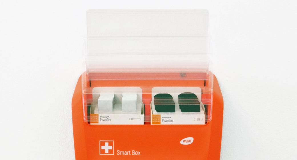 Orange WERO Smart Box mit zwei Fächern, gefüllt mit einzeln verpackten PowerTex Pflastersets, beschriftet mit rotem Kreuz und WeroSoft Marke.