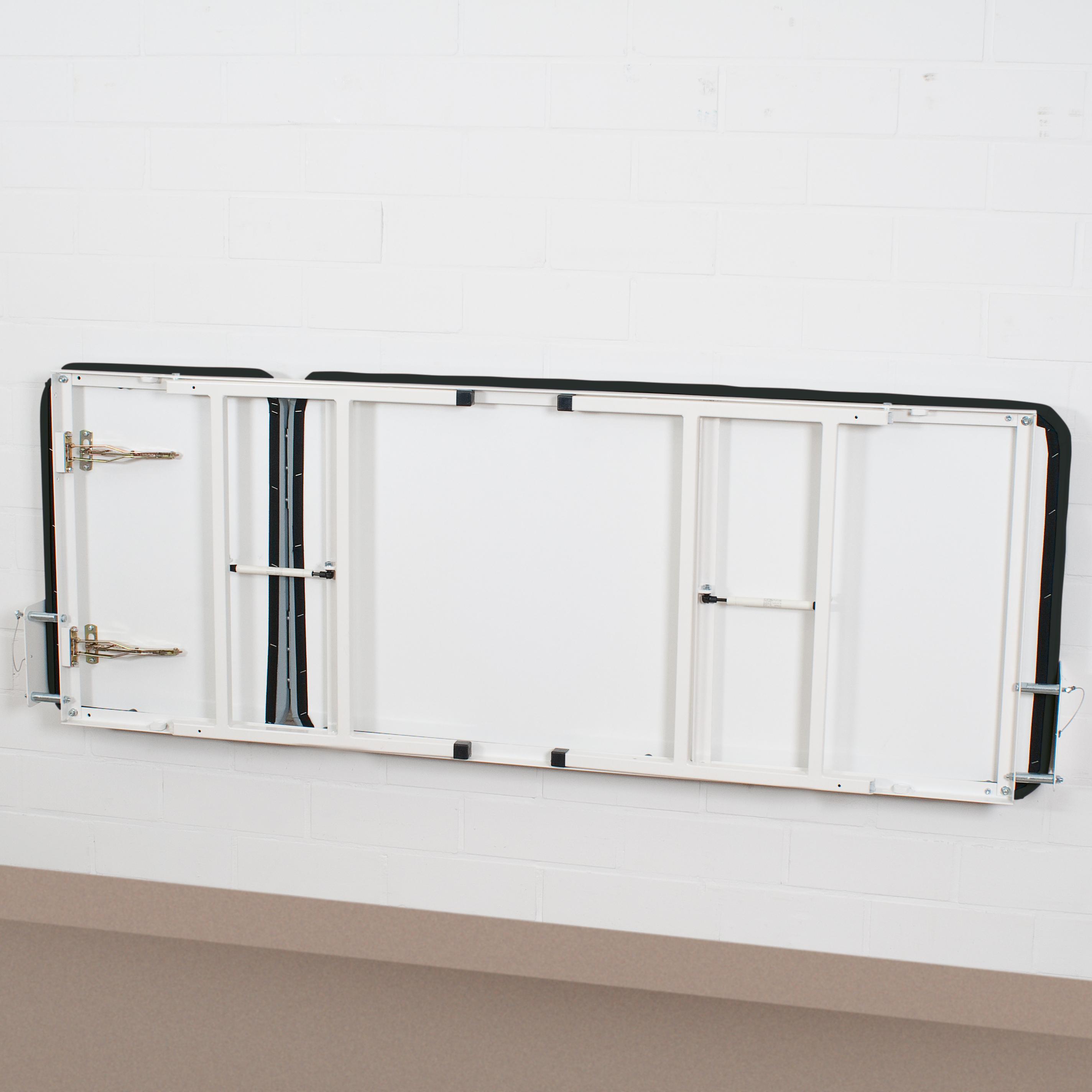 Eine teilweise ausgeklappte Wandklappliege - Schwarz aus weiß lackiertem Metall mit schwarzen Kanten und vier Scharnieren lehnt an einer weißen Backsteinwand.