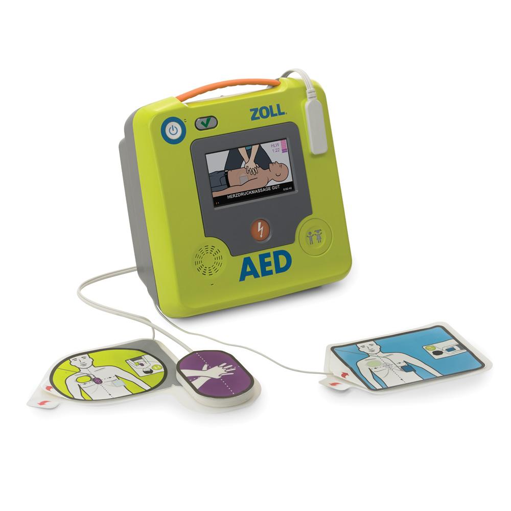 Grünes AED Defibrillator-Gerät mit Display, das eine Anleitung zeigt, und zwei angeschlossenen farbigen Elektrodenpads, angeschlossen an ein Stromkabel.