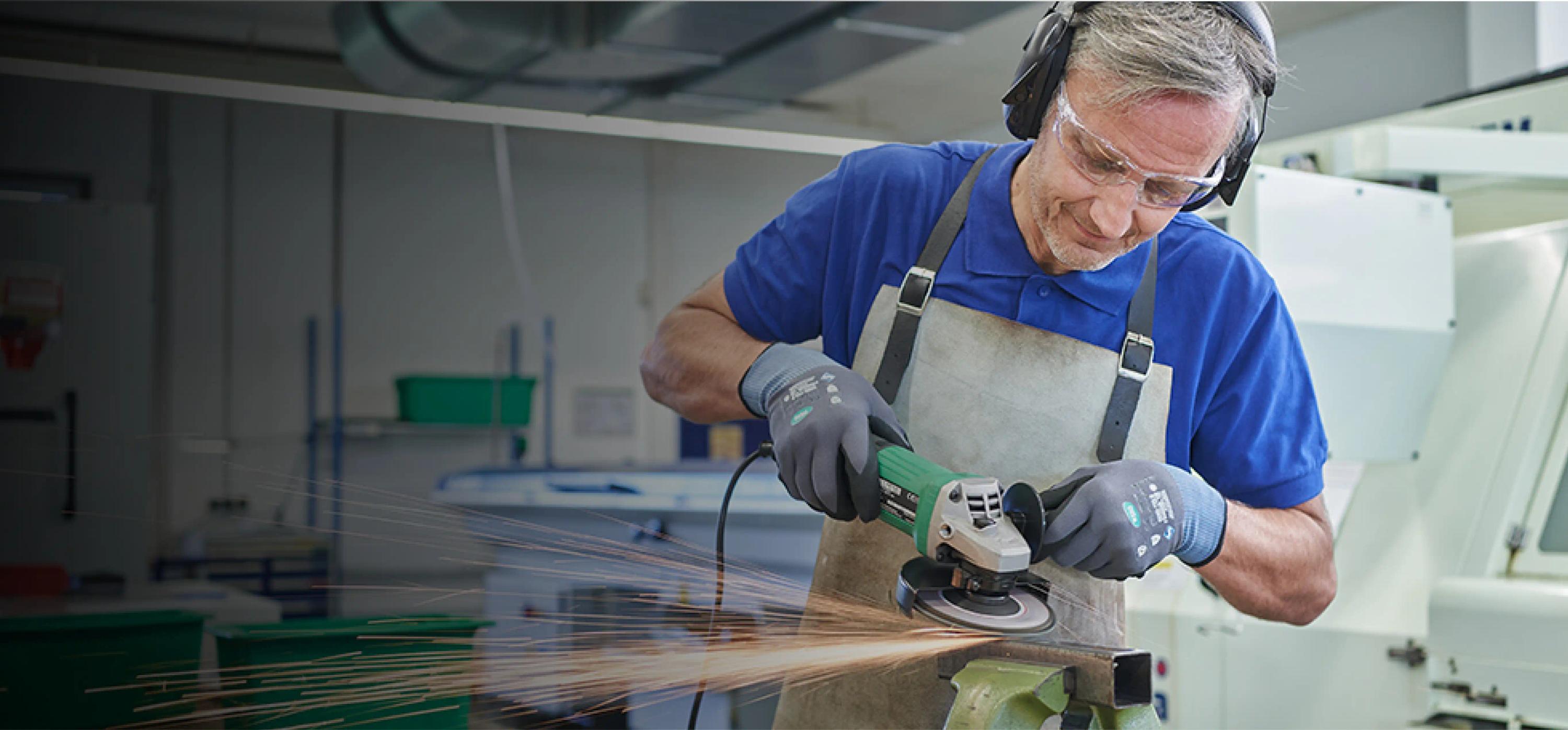 Ein Mann ,augestattet mit diverser Schutzkleidung, flext an einem Metallteil