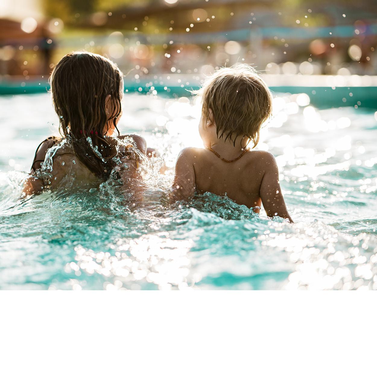 Zwei Kinder planschen im Wasser. Sie sitzen mit den Rücken zur Kamera