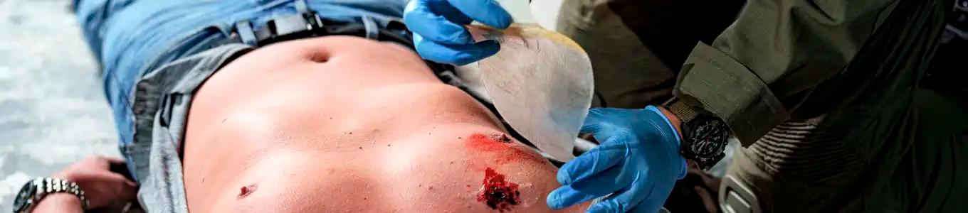Eine Hand mit grauem Arbeitshandschuh greift nach vier nebeneinanderliegenden weißen Handschuhen auf einer Holzwerkbank.