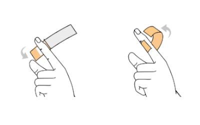 Eine Hand drückt mit Daumen und Zeigefinger auf ein rechteckiges, pfirsichfarbenes Objekt sowie auf ein ähnliches Objekt mit oranger Bandschleife.